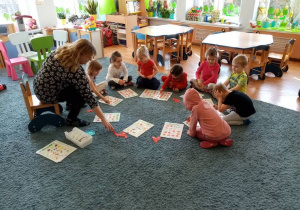 Dzieci na dywanie grają z nauczycielką w bingo.